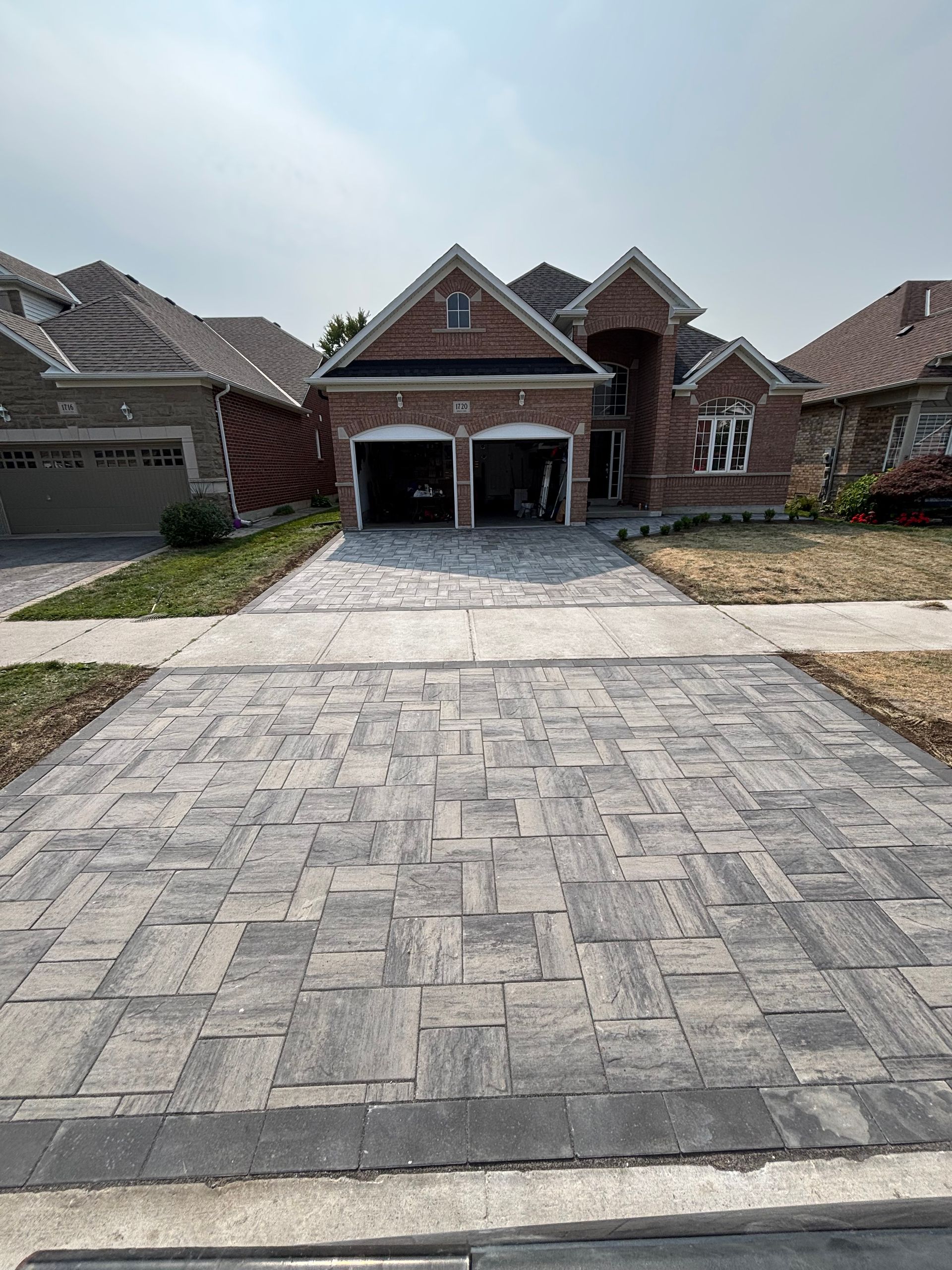 Brick home with two-car garage, brick driveway, and surrounding houses on a sunny day.