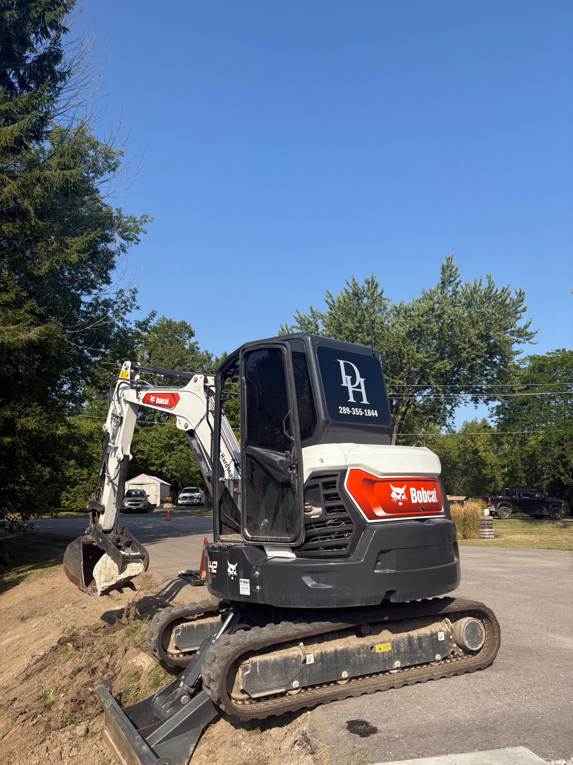 White and black Bobcat excavator on a paved lot with trees and blue sky in the background.