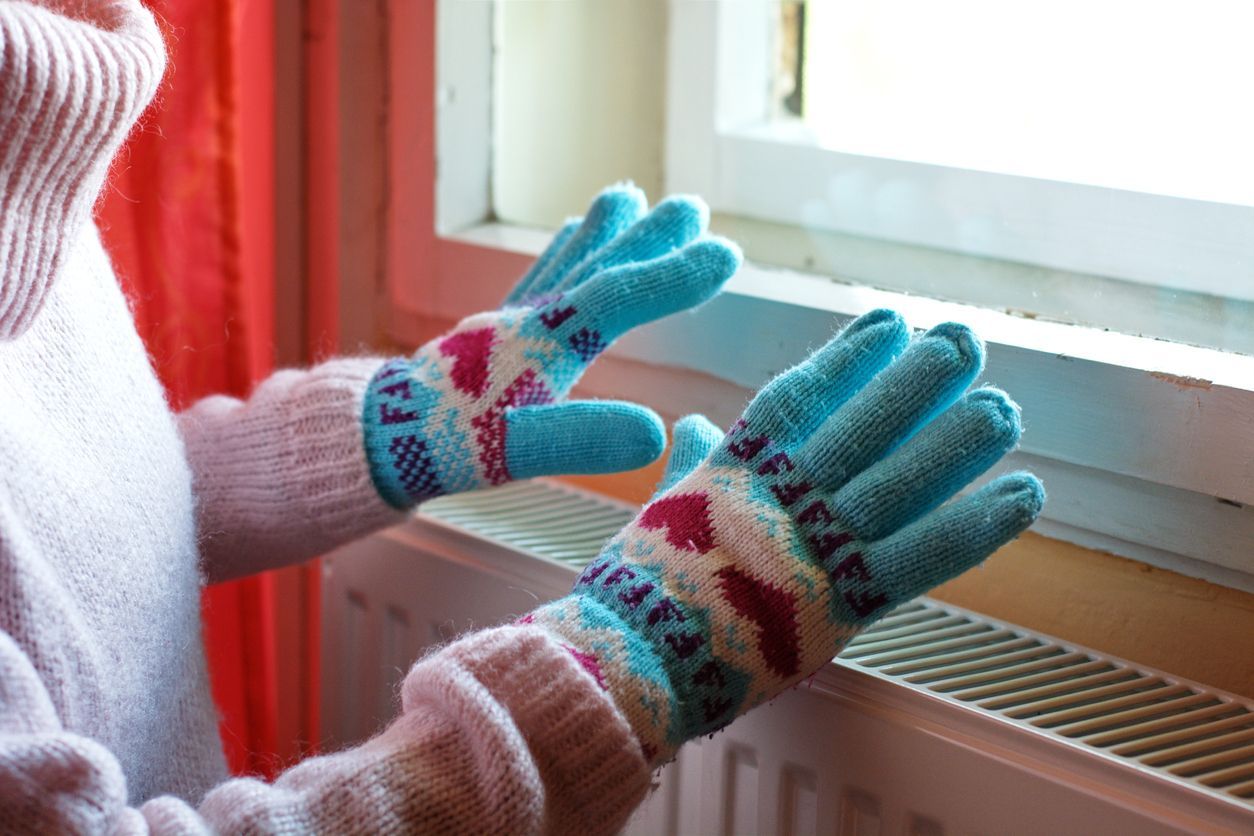 A woman hands in wool gloves warms near the heater.