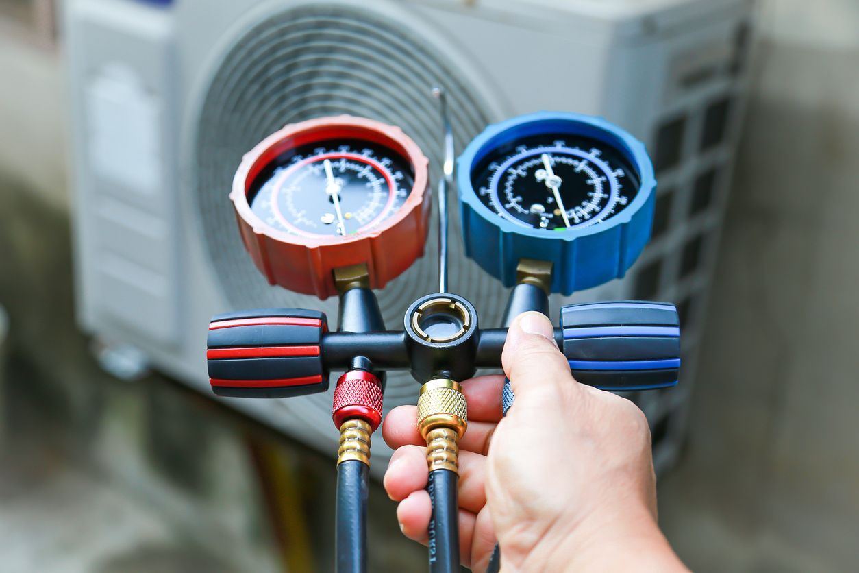 A Gibson Heating & Cooling technician is holding two gauges in front of an air conditioner.