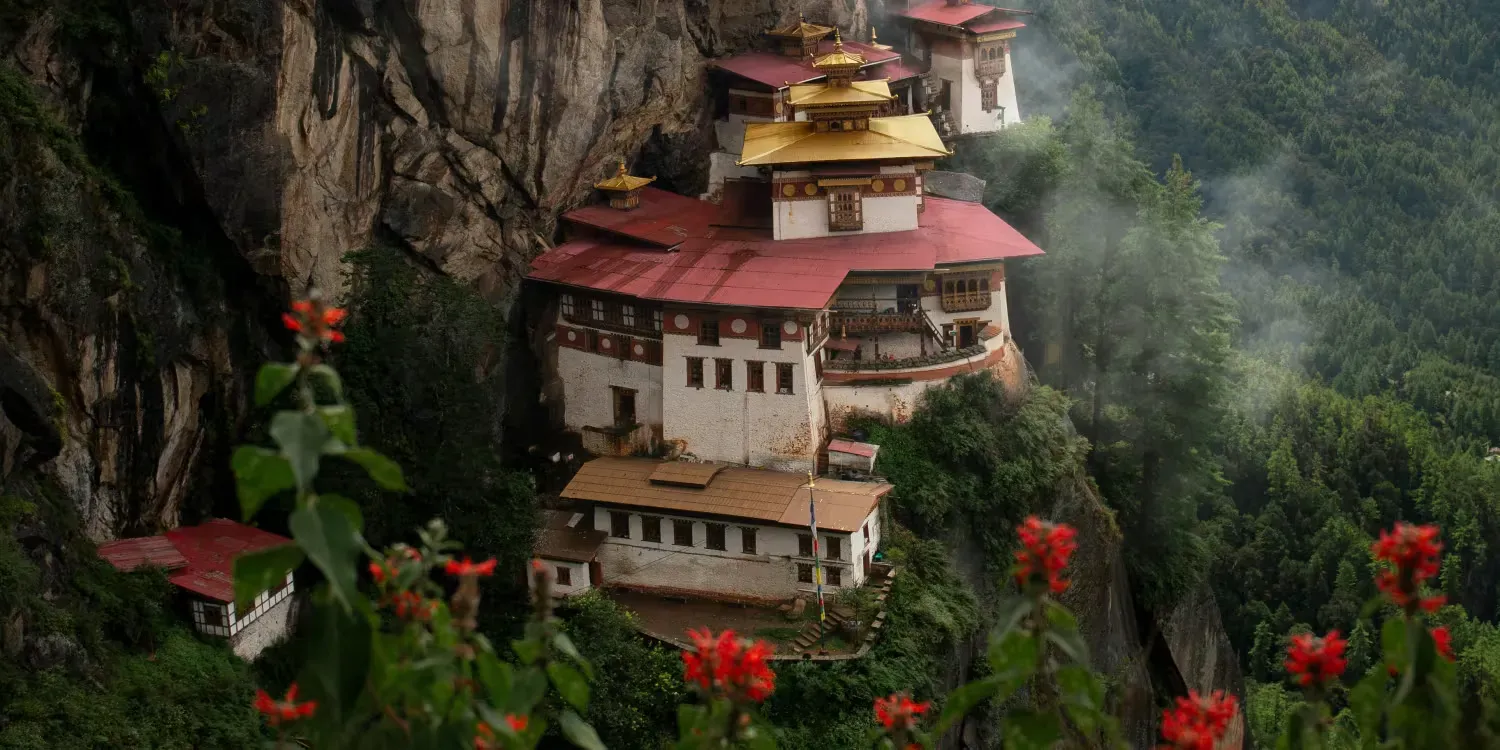 Mountain monastery with red roofs nestled in a rocky cliff, surrounded by mist and flowers