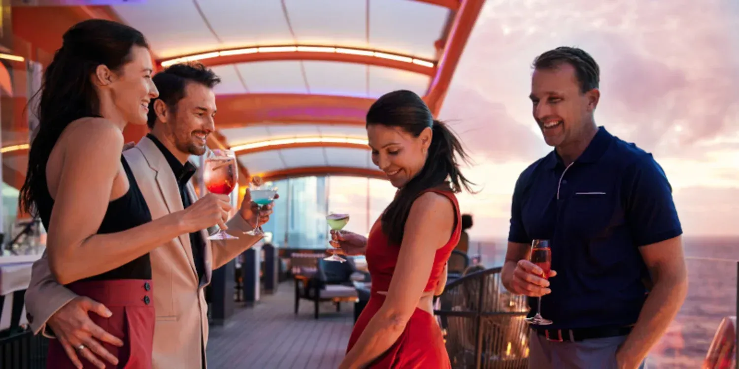Four adults chatting with drinks in a warmly lit lounge with a curved ceiling and sunset glow