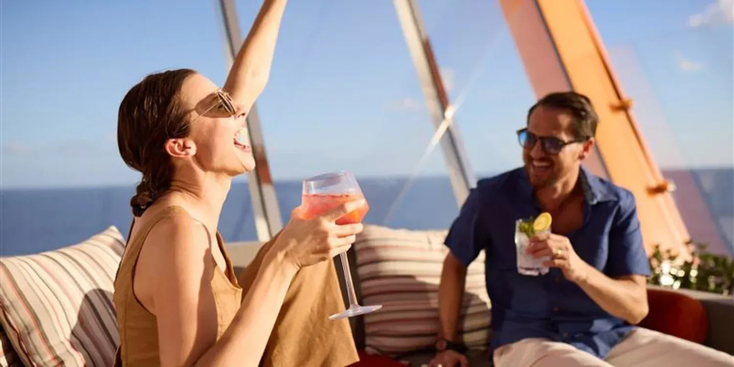 Two people relaxing on a boat deck, smiling and drinking cocktails by the sea.