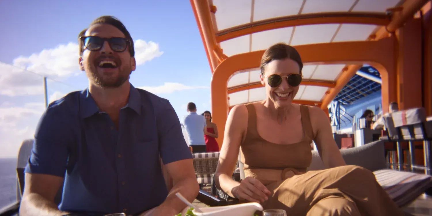 Two people sitting on a boat deck in sunglasses, smiling in the sun.