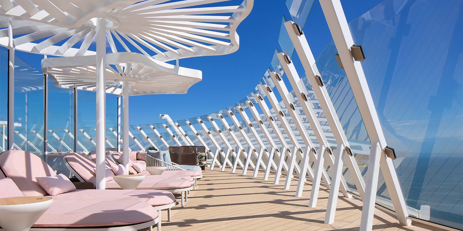 Beachside lounge area with white parasols, pink sunbeds, and glass wall overlooking the ocean.