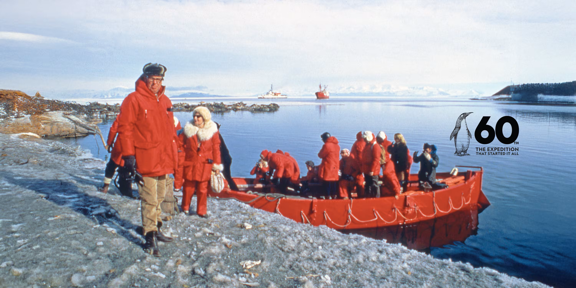 People in red parkas load into a red boat in Antarctica; the sea and a ship are in the background.