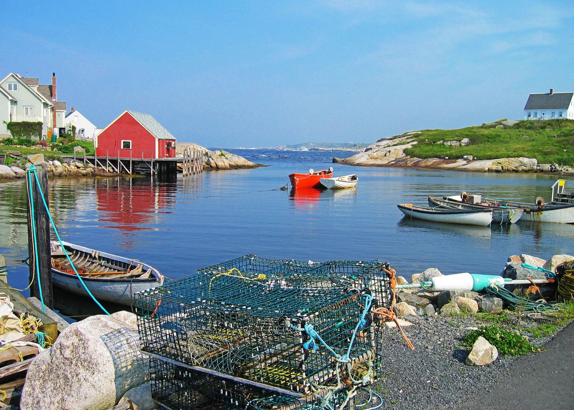 A colorful harbor with a red building on stilts, small fishing boats, and lobster traps along the rocky shore.