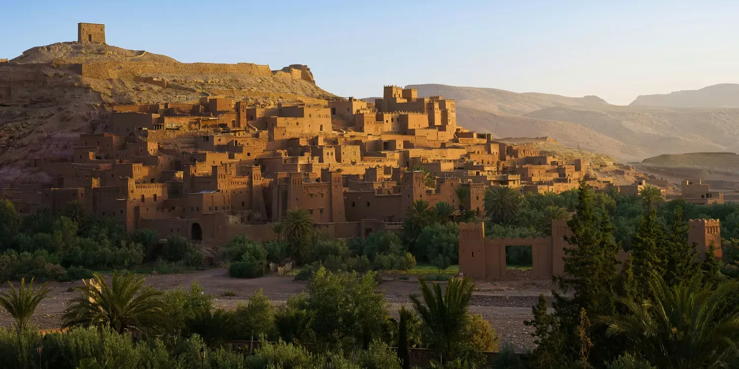 Sunlit hillside village of stone buildings and a hilltop fortress at dusk