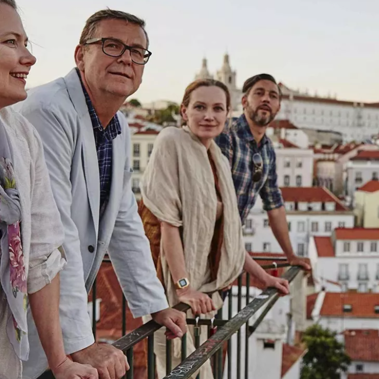 A family looks out from a balcony overlooking orange-tiled rooftops in Spain.