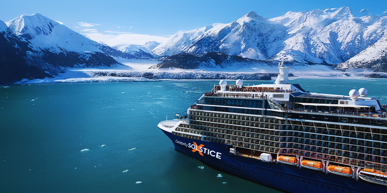 Cruise ship sailing on blue water in front of snow-covered mountains.