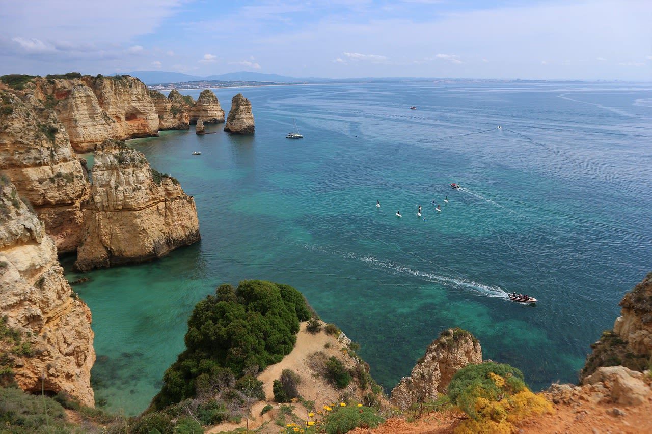 High-angle view of turquoise water along rugged, golden limestone cliffs in the Algarve, Portugal, with boats nearby.
