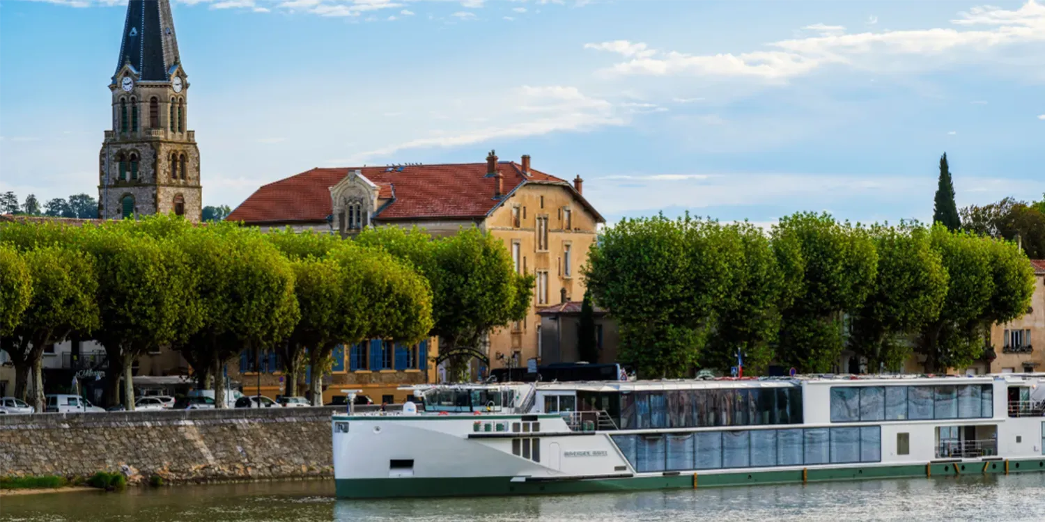 A river cruise ship docked by a city with a church steeple.