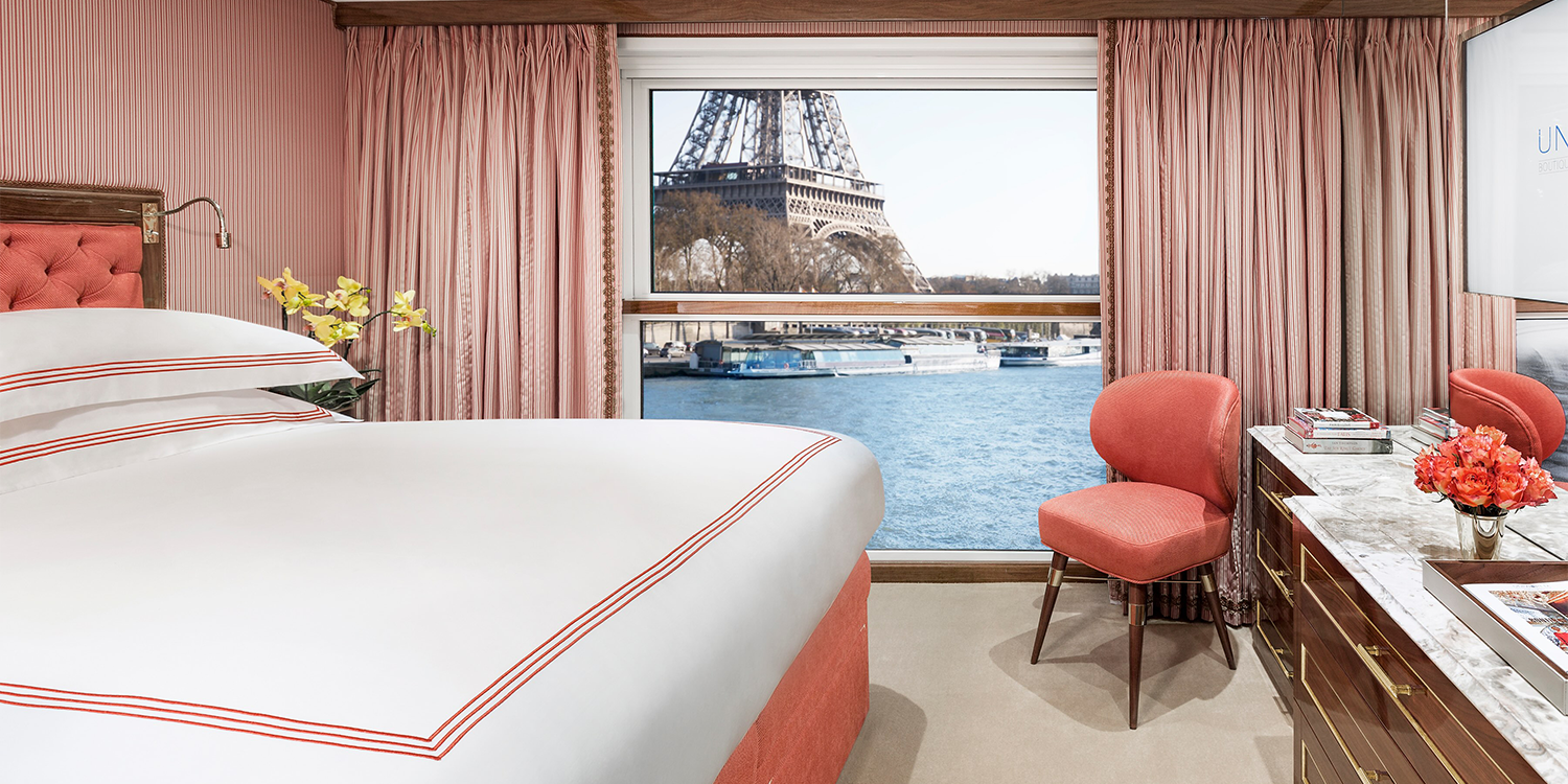 Bedroom with a view of the Eiffel Tower through a window. Pink curtains, bed, and chair.