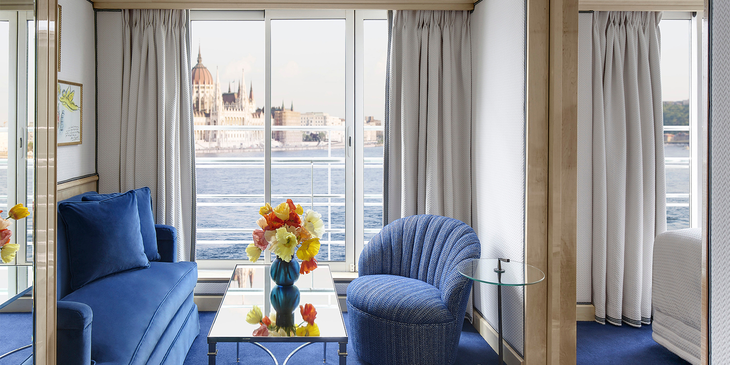 Luxurious blue-themed room with a river view. Includes a blue couch, chair, and a table with flowers.