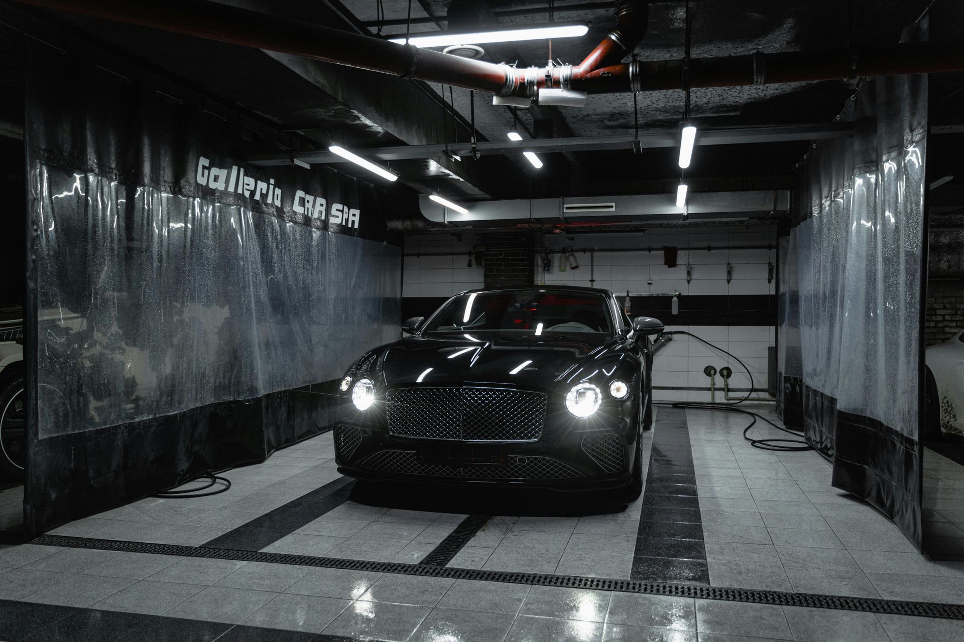 Black Bentley inside a car wash bay, water spraying.