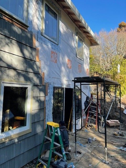A man sits on a ladder in front of a house under construction