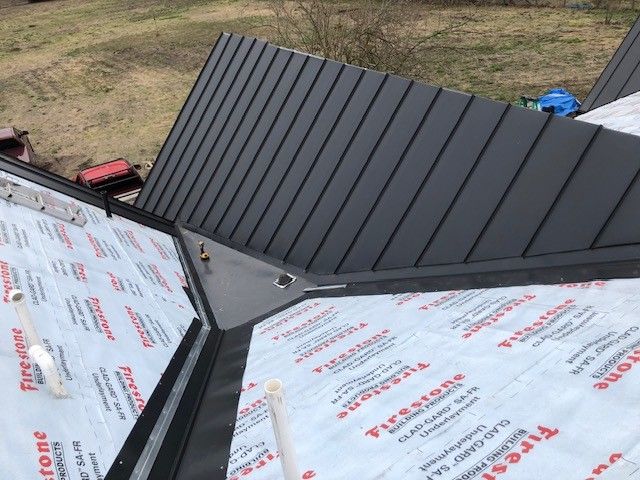A black metal roof is being installed on a house