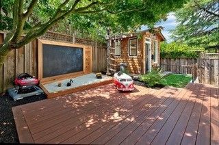 A wooden deck with a sandbox and a chalkboard in the backyard.