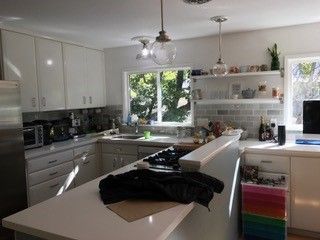 A kitchen with white cabinets , a stove , a refrigerator , a sink , and a window.