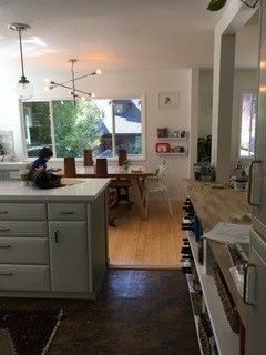 A kitchen with white cabinets and a wooden counter top leading to a dining room.