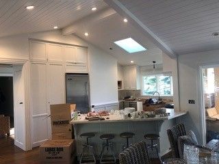 A kitchen with white cabinets , stools , a refrigerator and a skylight.