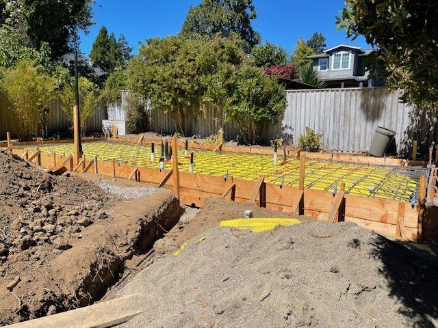 A construction site with a house in the background and a pile of dirt in the foreground.