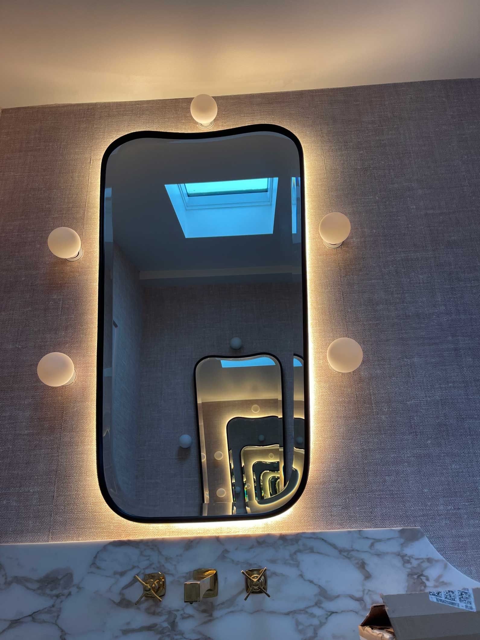 A bathroom mirror with lights behind it and a skylight.