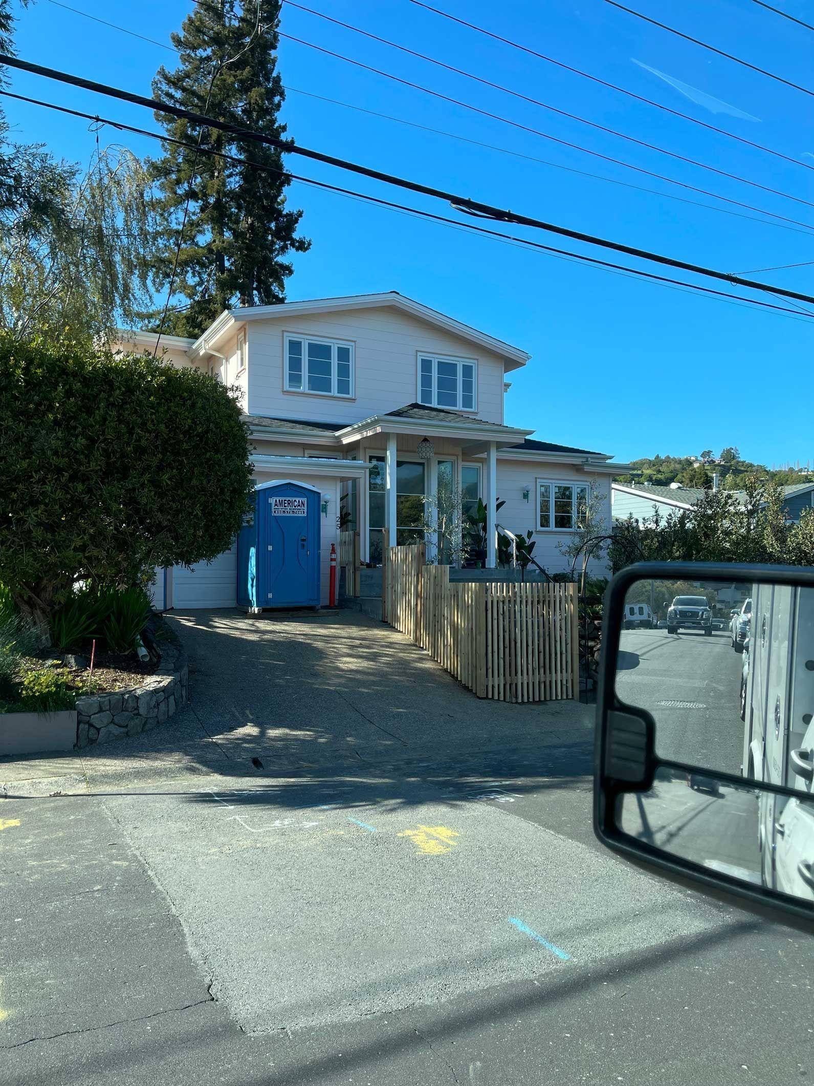 A white house with a blue door is visible in the rear view mirror of a car.