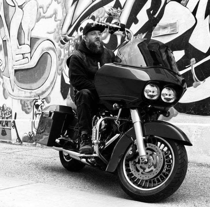 A man is riding a motorcycle in front of a graffiti wall.