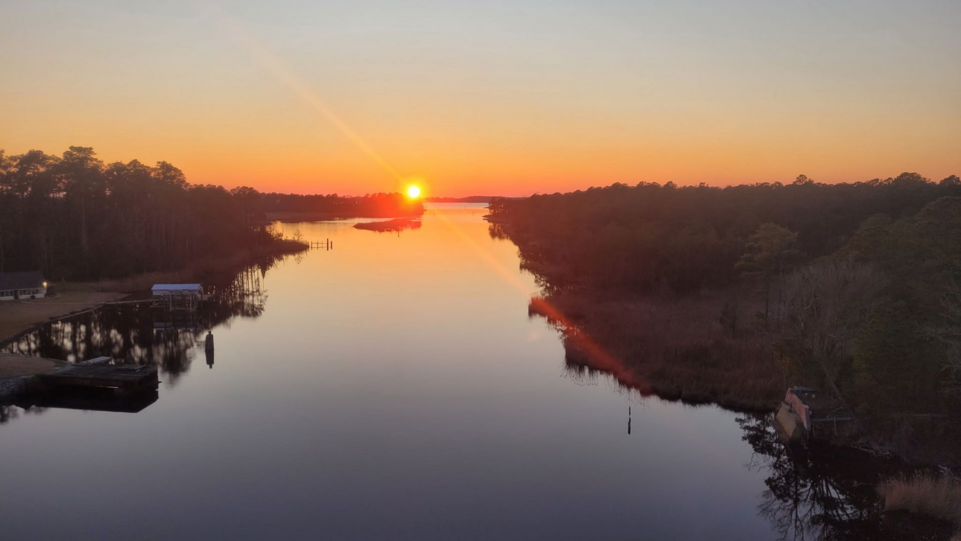 Sunset over a calm river, with silhouetted trees and a glowing orange sky