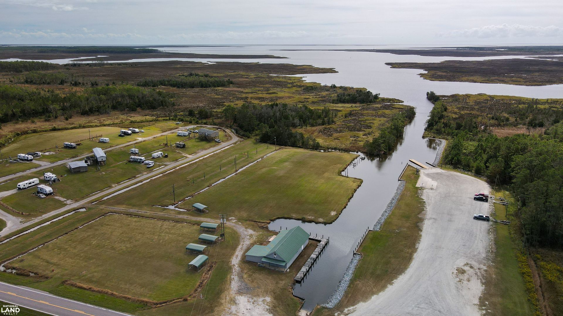 Aerial view of a riverside campground with cabins, gravel roads, and water channels through green wetlands.