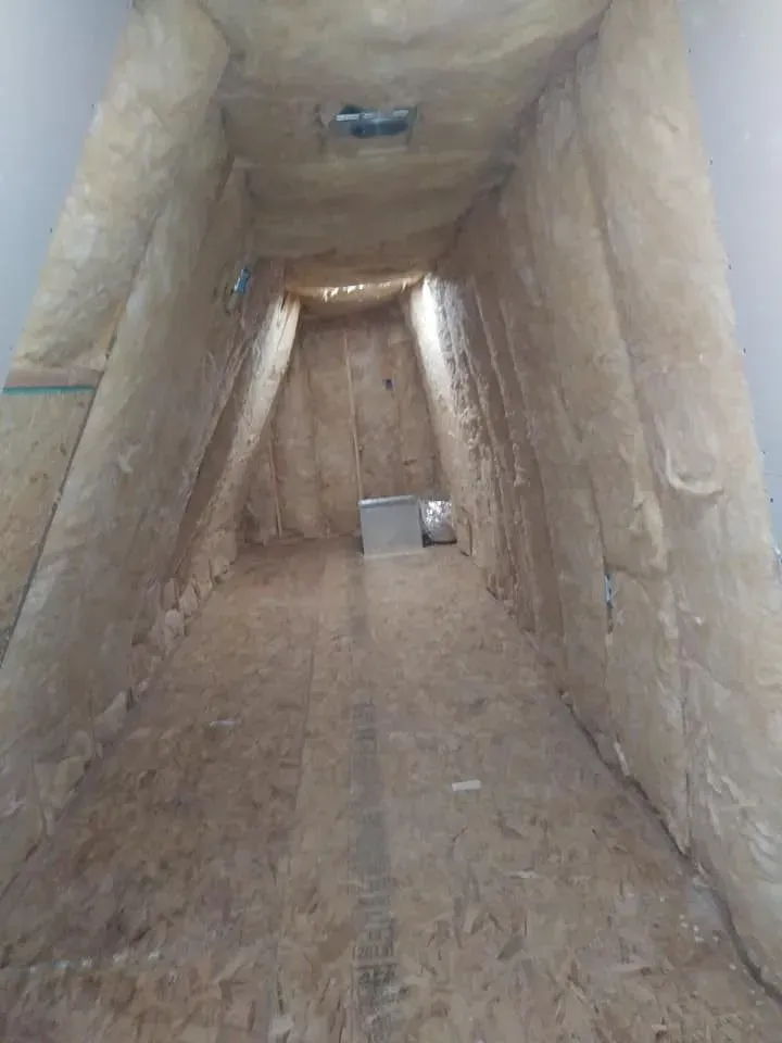 Attic space with wood floor, insulation on walls, and small vent in the ceiling.