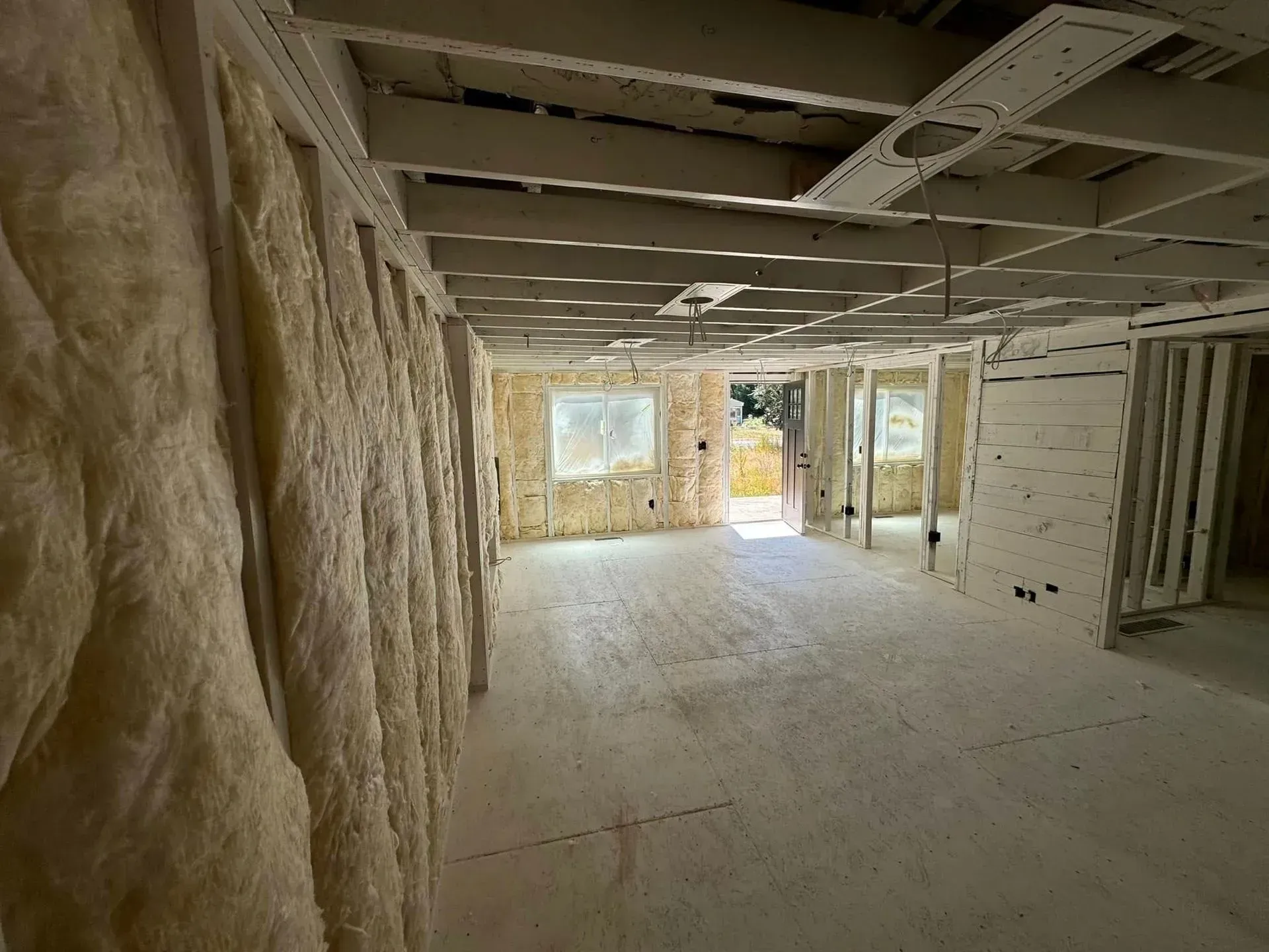 Interior of a building under construction, showing insulation on walls, open doorways, and exposed ceiling beams.