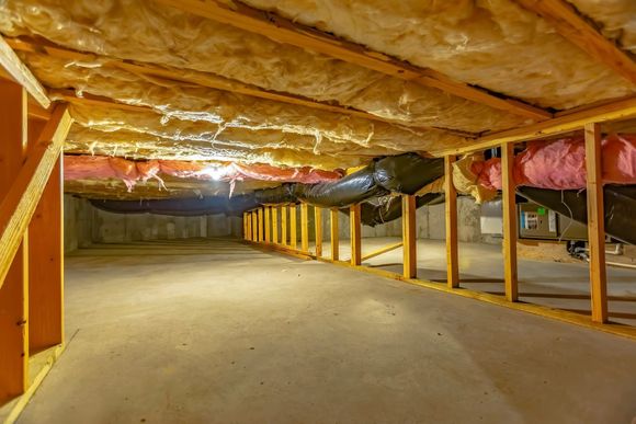 Crawlspace with wooden beams, insulation, and ductwork. Concrete floor, low angle.