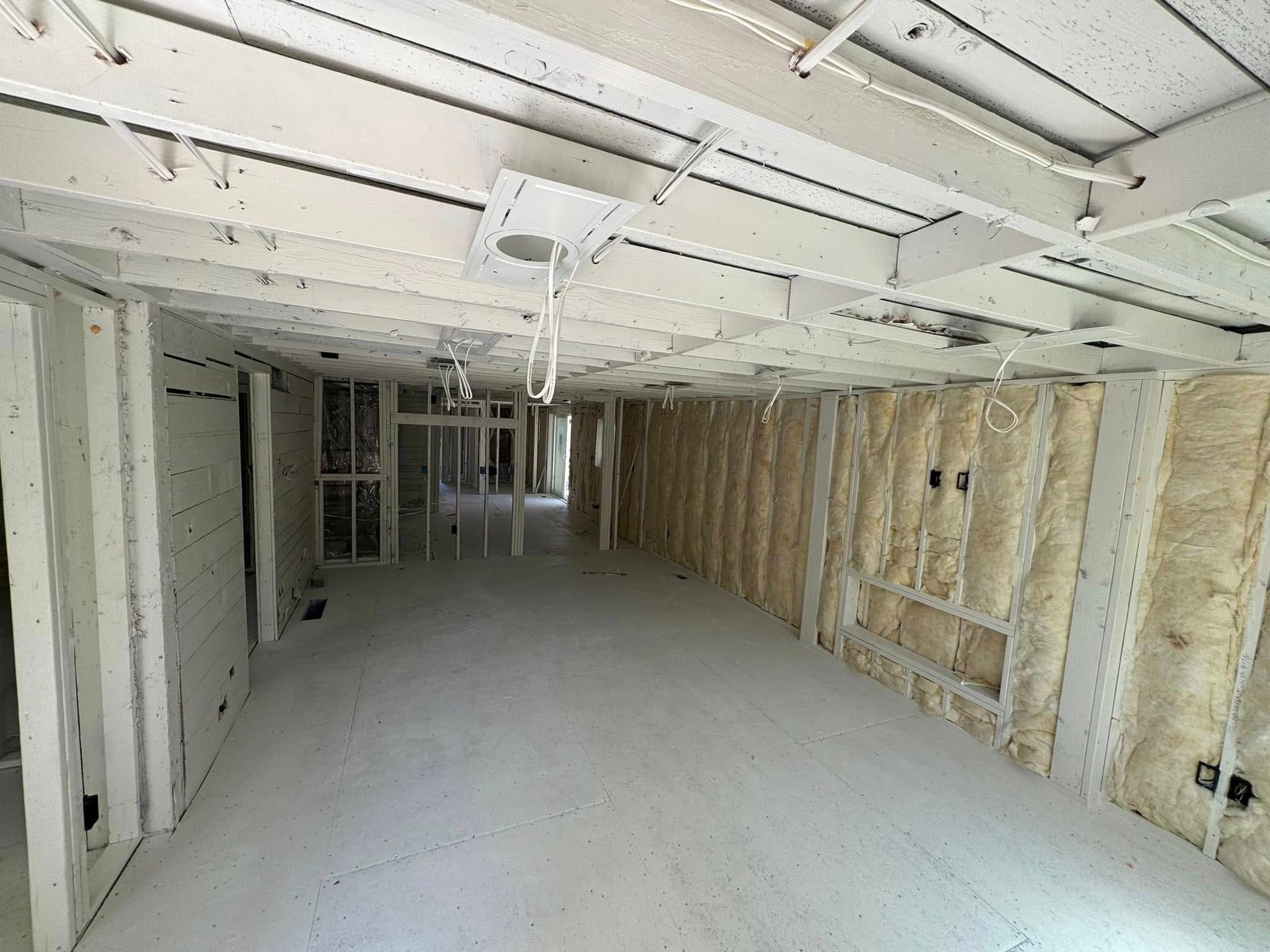 Interior of a building under construction; white walls and ceiling, insulation visible, concrete floor.