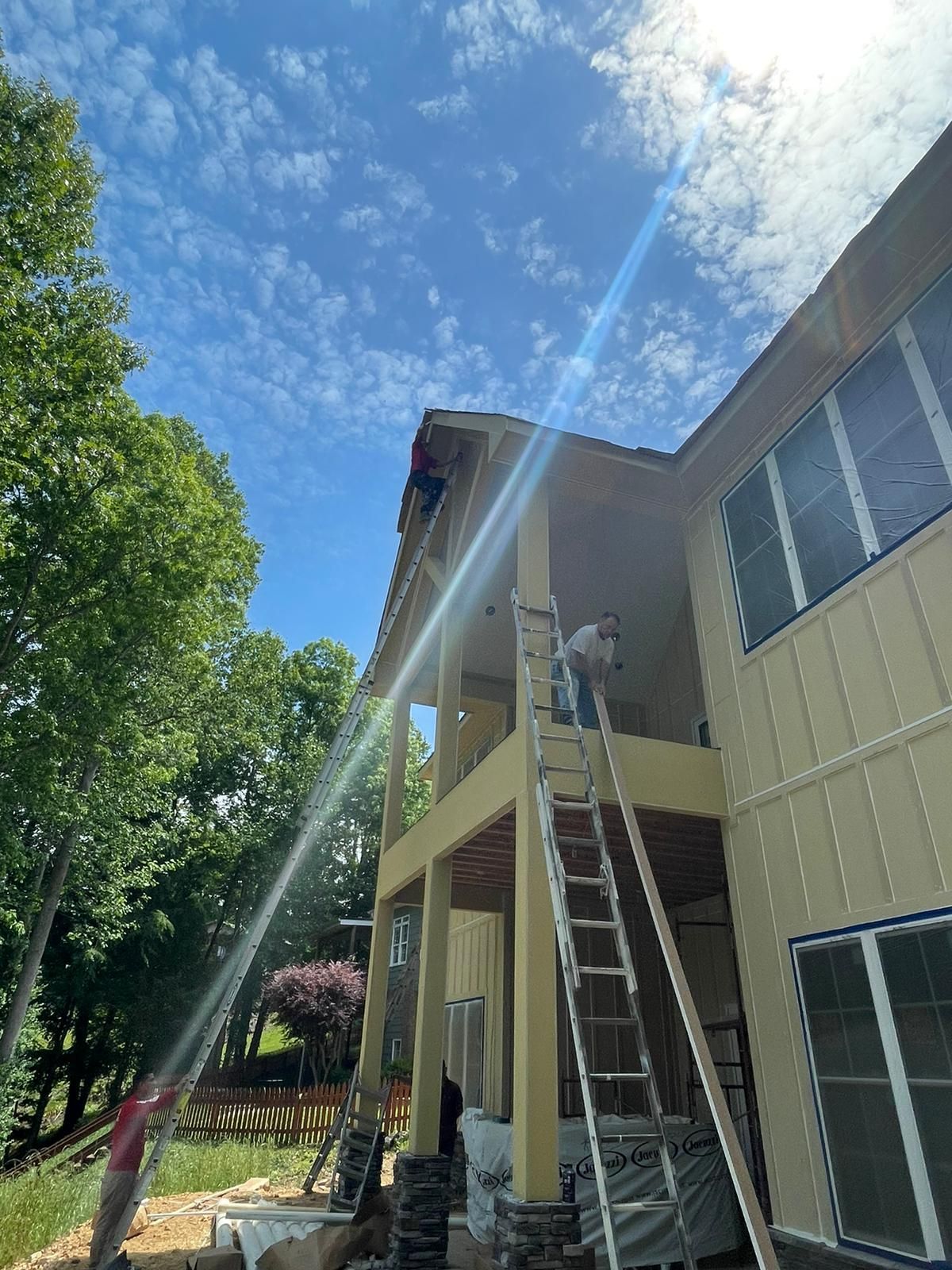 A man is painting the roof of a house with a ladder.