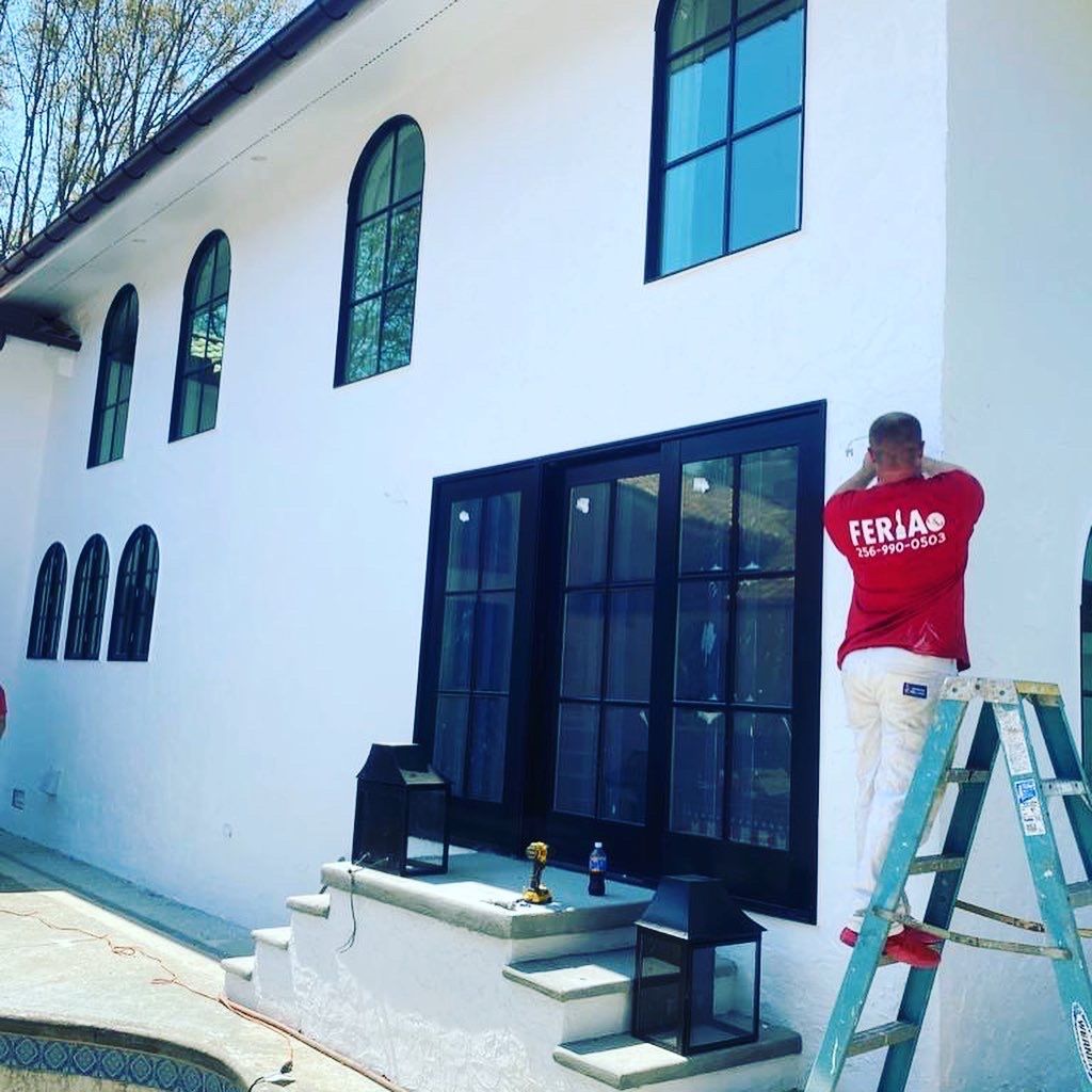 A man is standing on a ladder painting a white building.