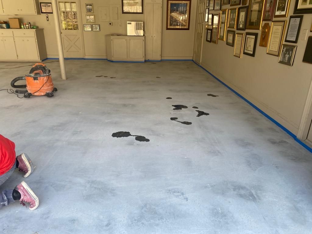 A person is kneeling on a concrete floor in a room with pictures on the wall.