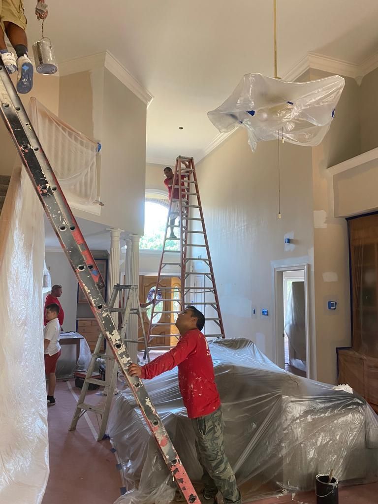 A man is standing on a ladder in a living room painting a wall.