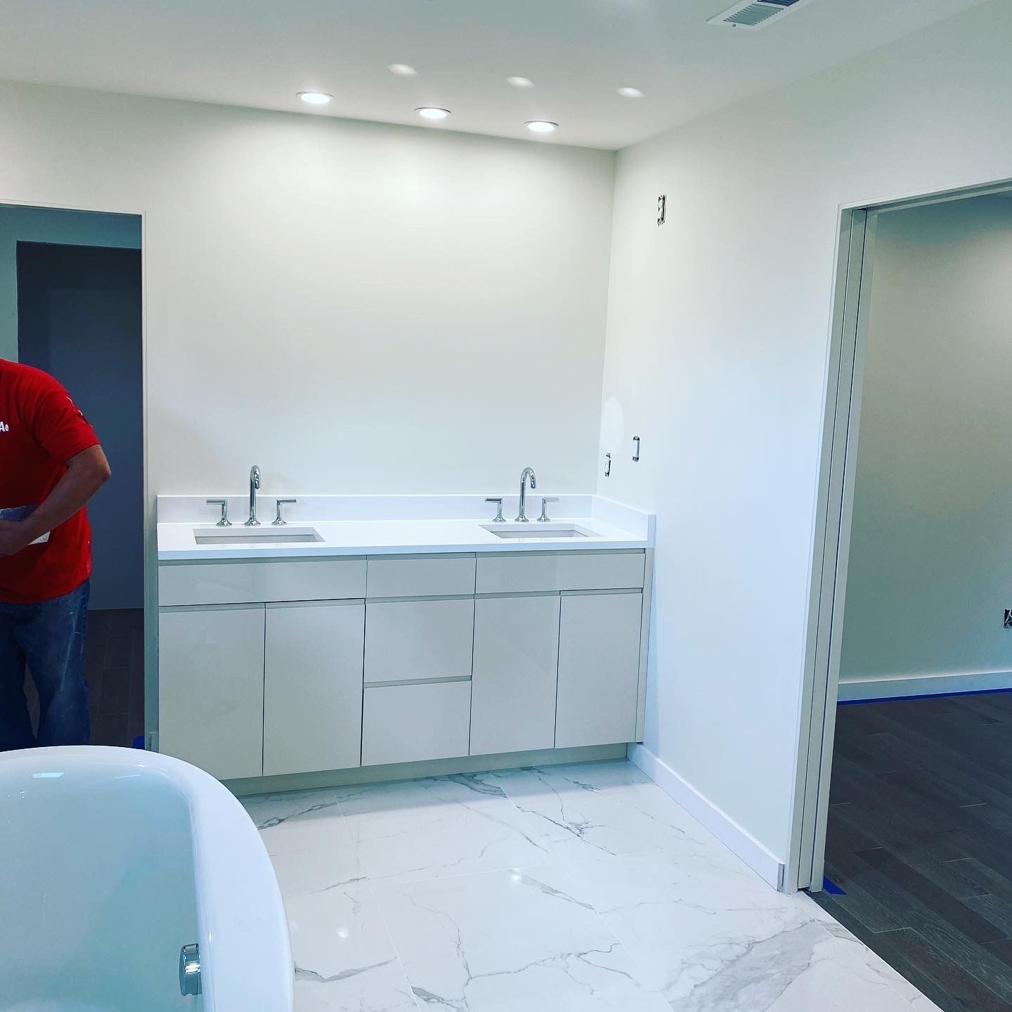 A man in a red shirt is standing in a bathroom next to a bathtub.