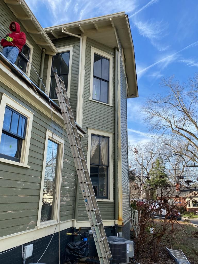 A man is standing on the roof of a house with a ladder.