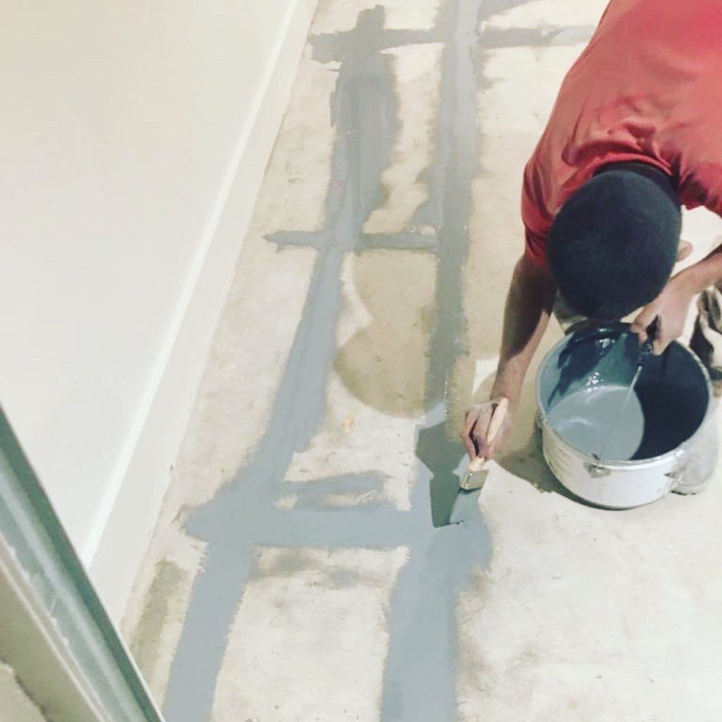 A man in a red shirt is painting the floor with a brush