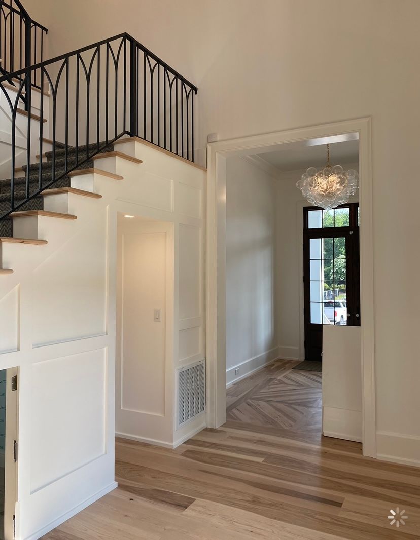 A hallway with stairs leading up to the second floor and a chandelier hanging from the ceiling.