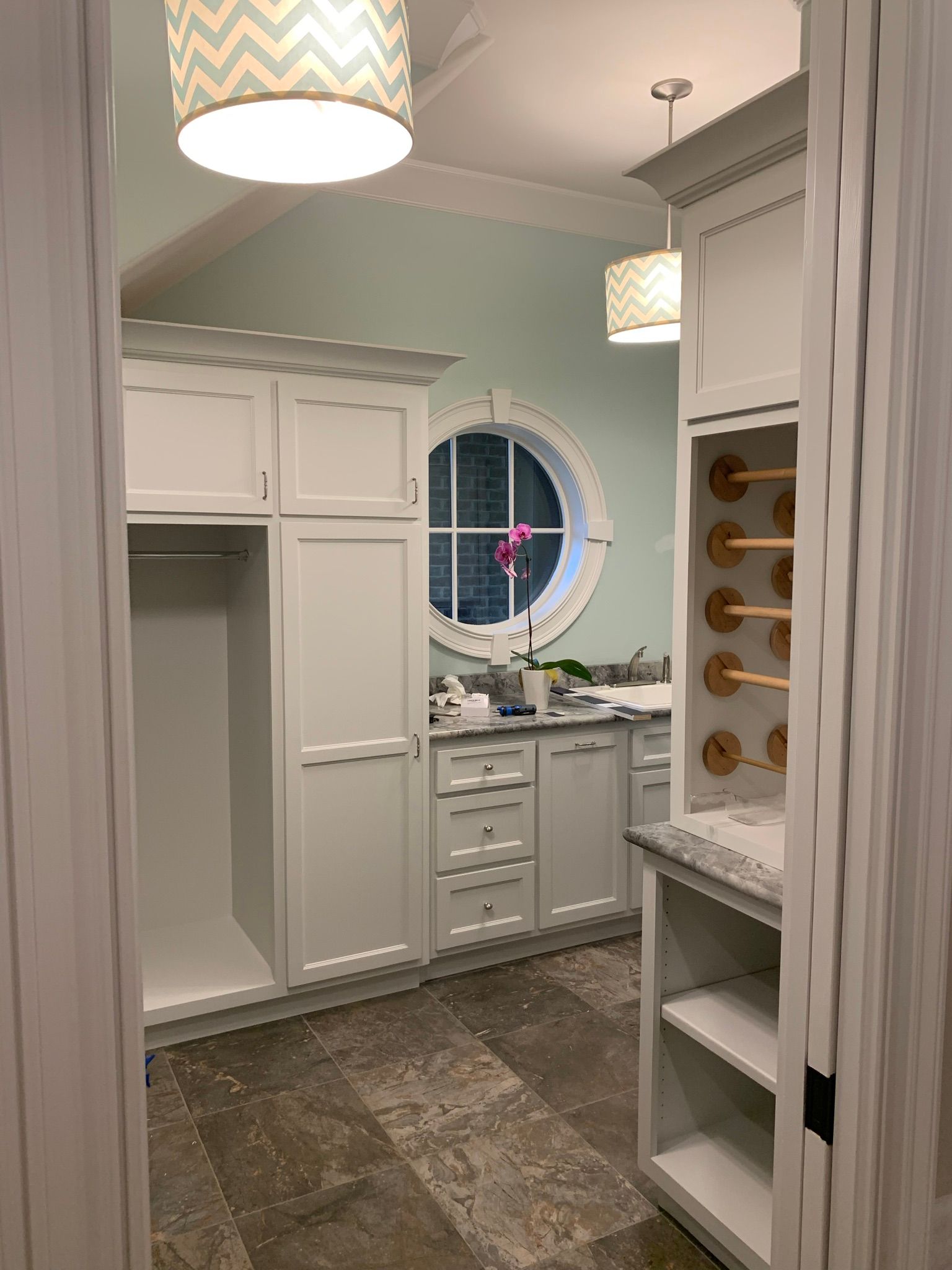A laundry room with white cabinets and a round window.