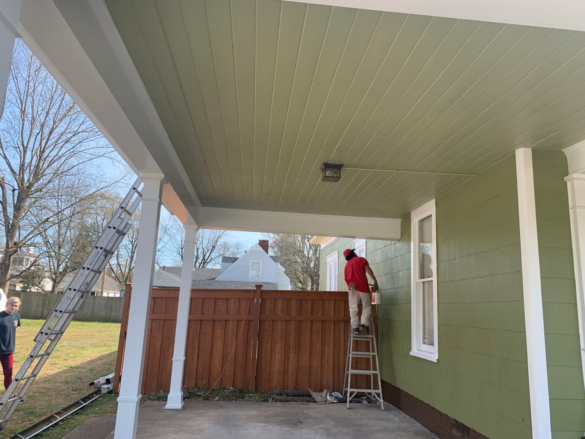 A man is painting the side of a green house.