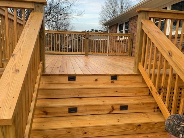 A man is standing on a wooden deck with stairs leading up to it.