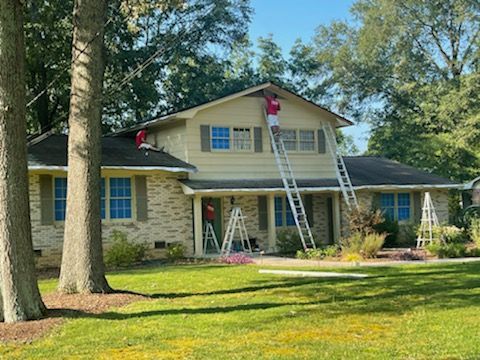 A man is standing on a ladder painting the roof of a house.