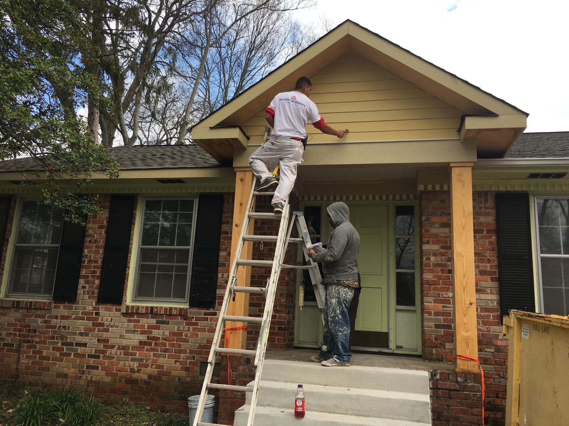 Two men are painting the front of a brick house.