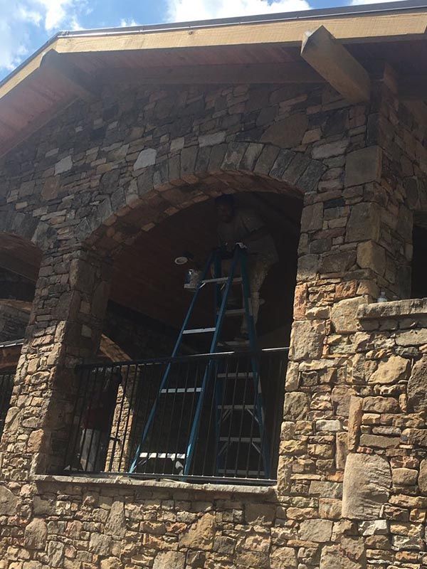 Man is Standing on a Ladder in Front of a Stone Building