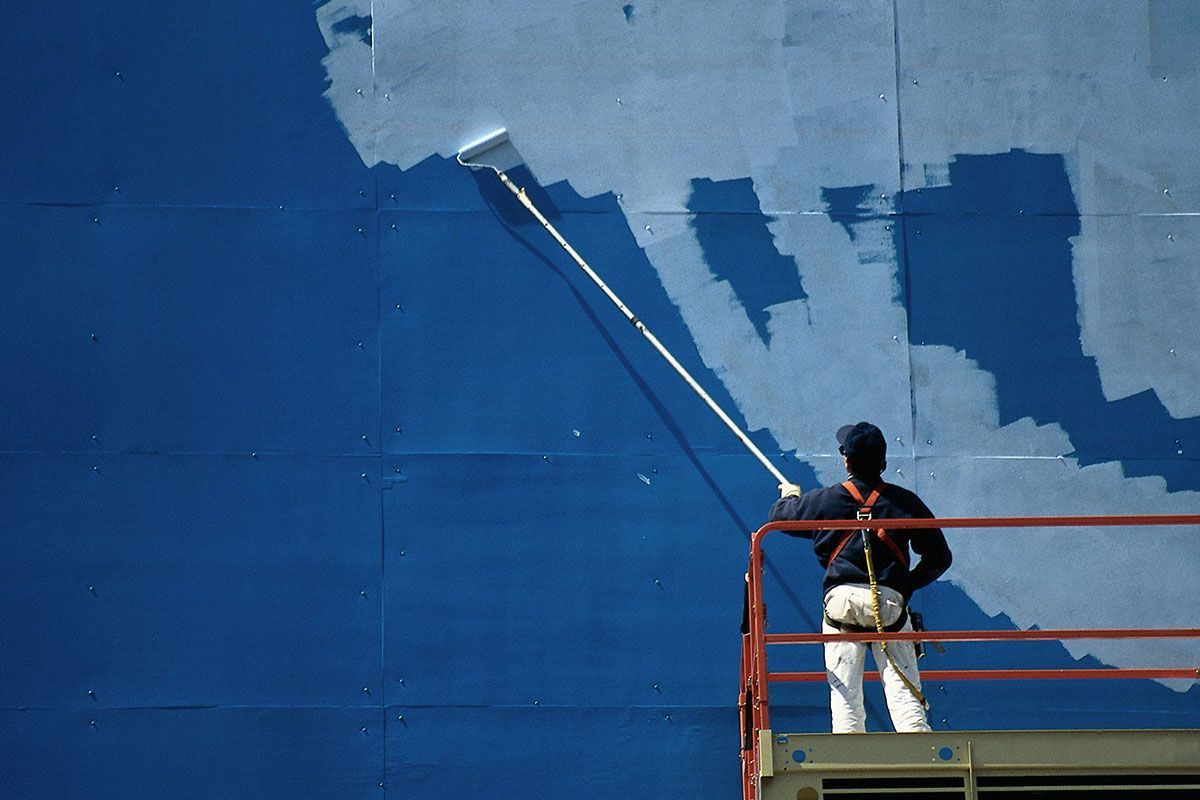 Worker Using Paint Roller Painting the Exterior of Building